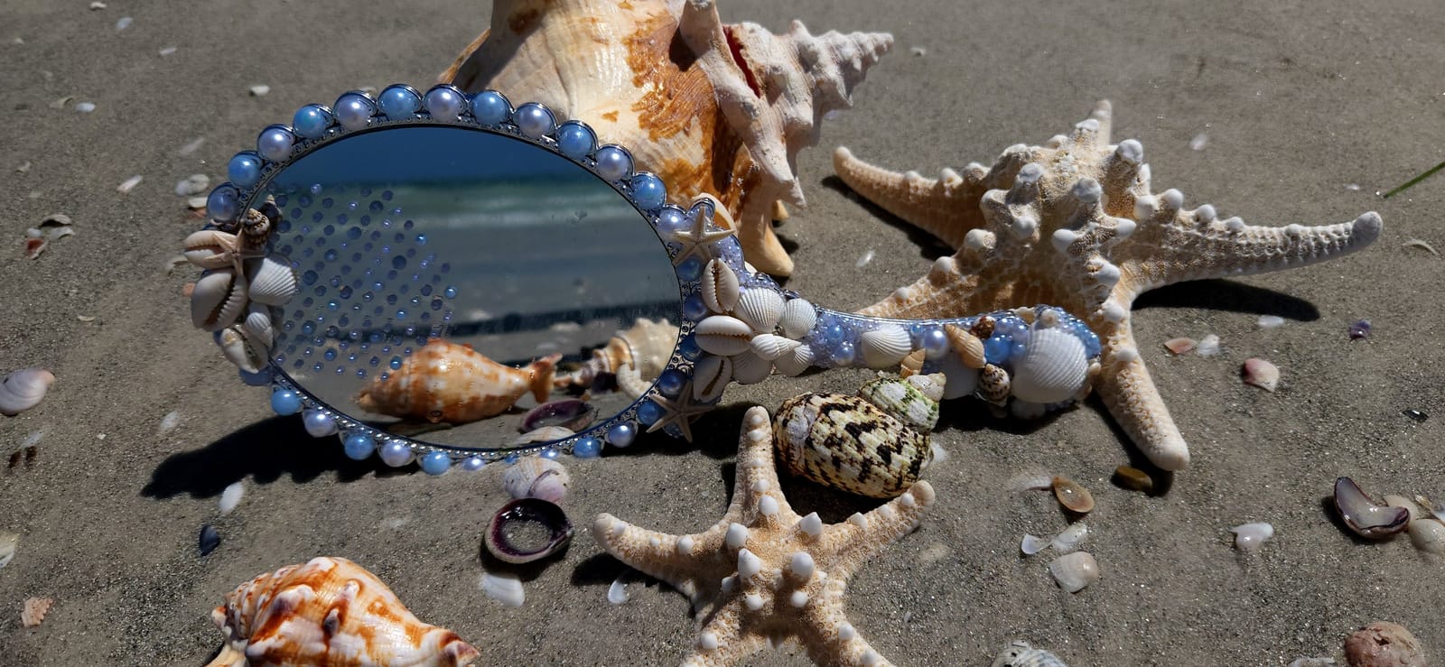 Espelho de mão Reflexo das Marés refletindo o mar, com moldura de conchas, pérolas azuis e estrela-do-mar sobre a areia
